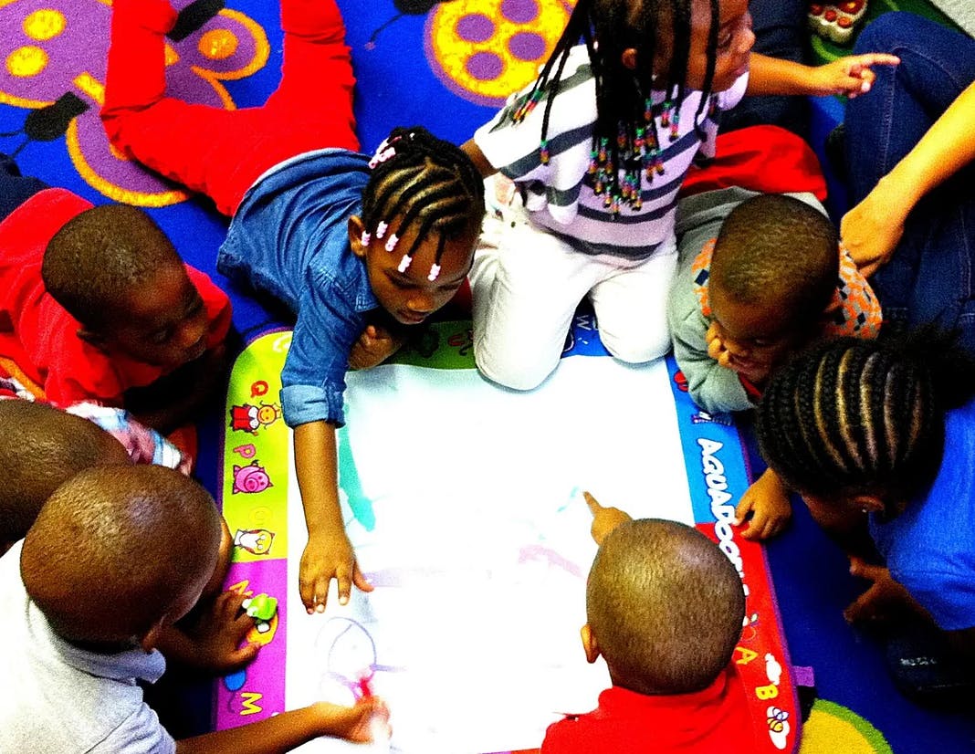 Children gathered around a white drawing mat