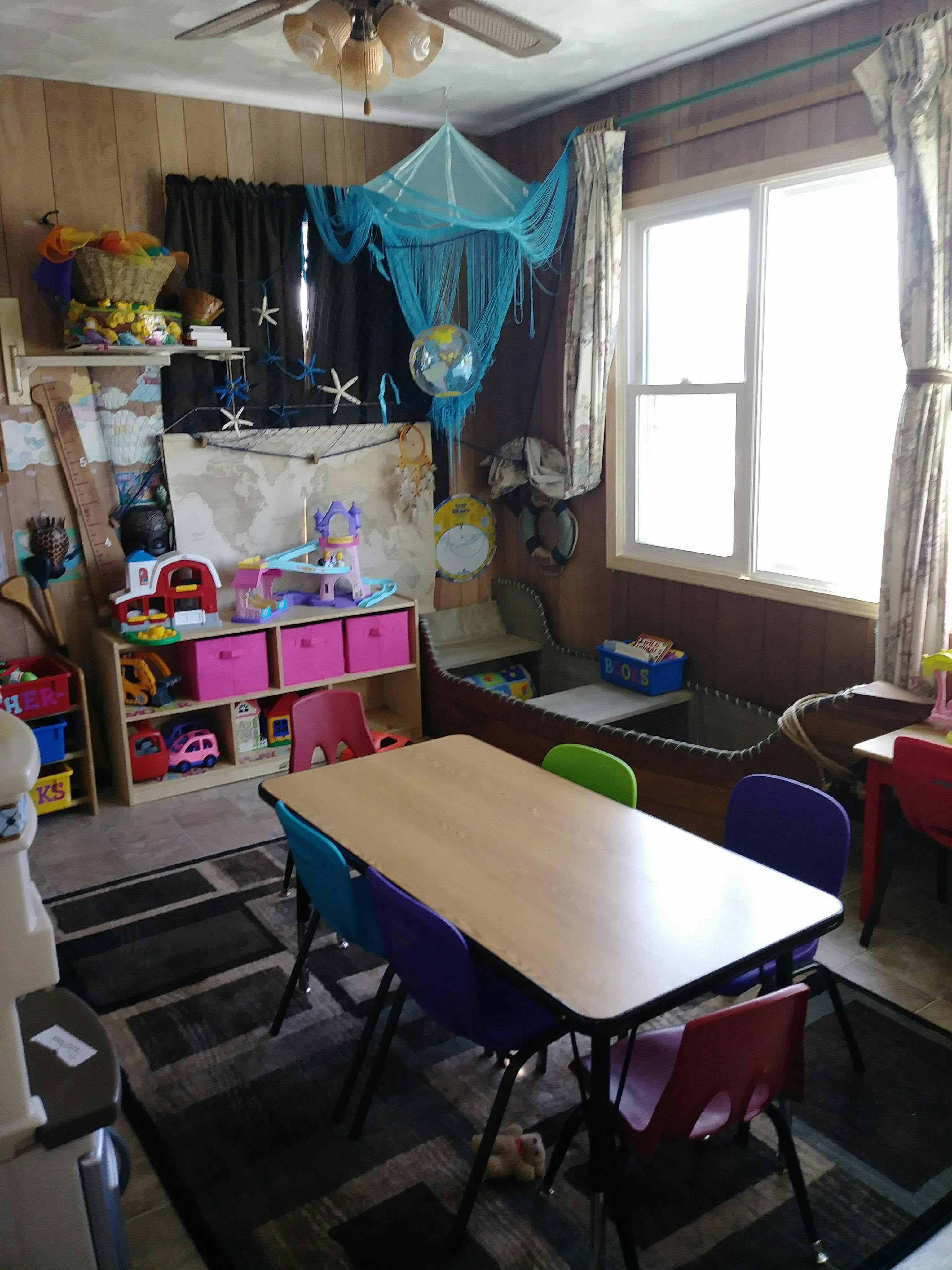 Classroom with a table and chairs, toys on shelves, and a window
