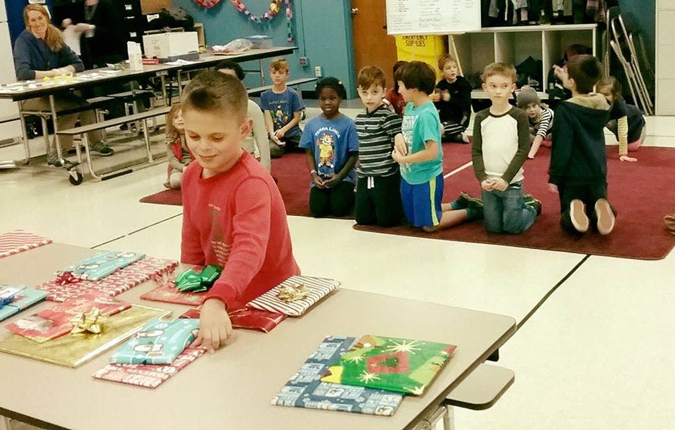 Child at a table with wrapped gifts, other children kneeling on a rug