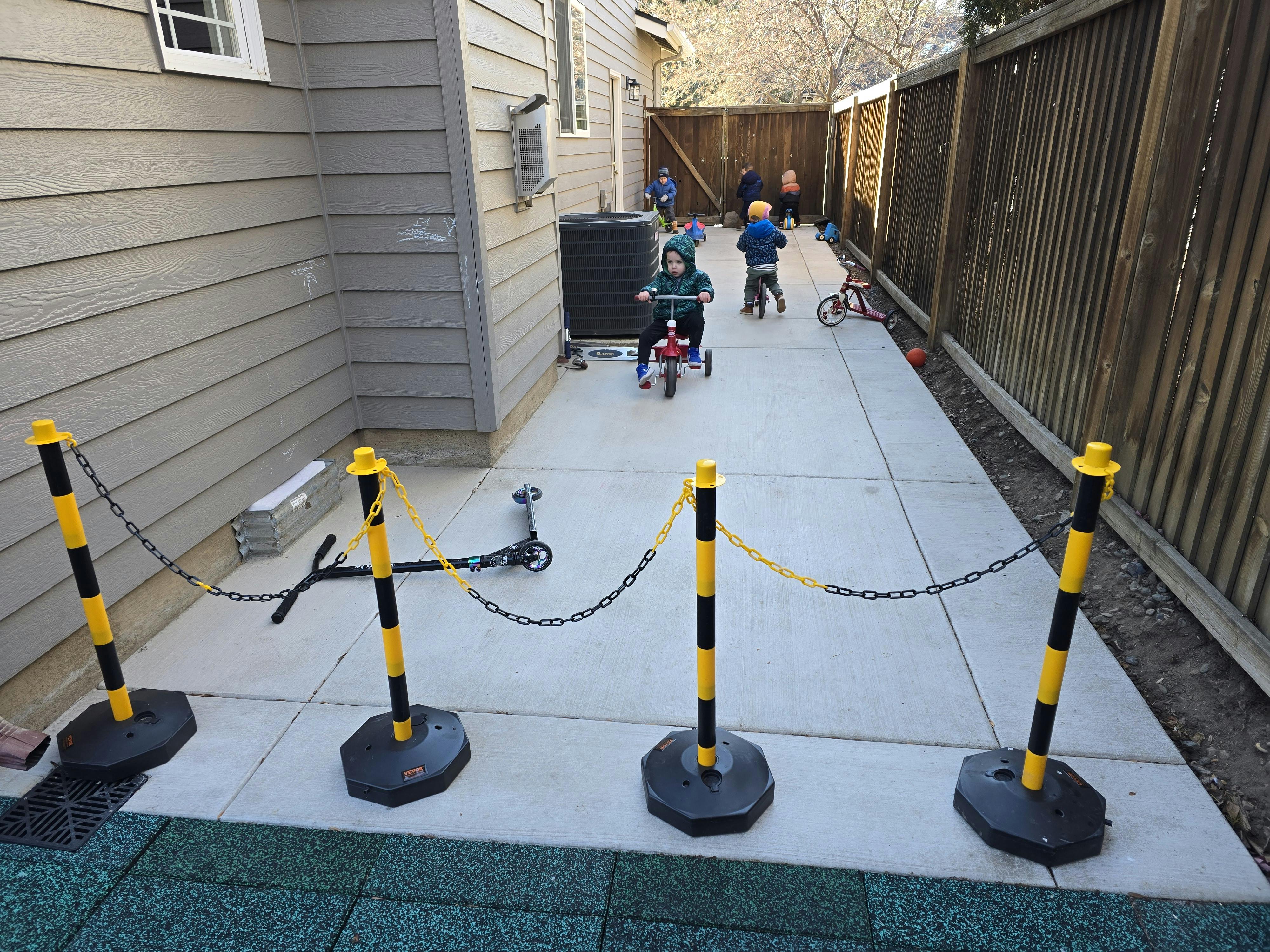 Children riding tricycles on a paved path next to a building