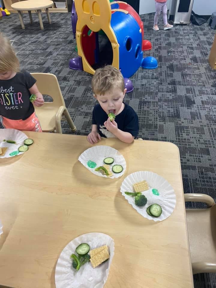 Child eating a piece of broccoli at a table with other children
