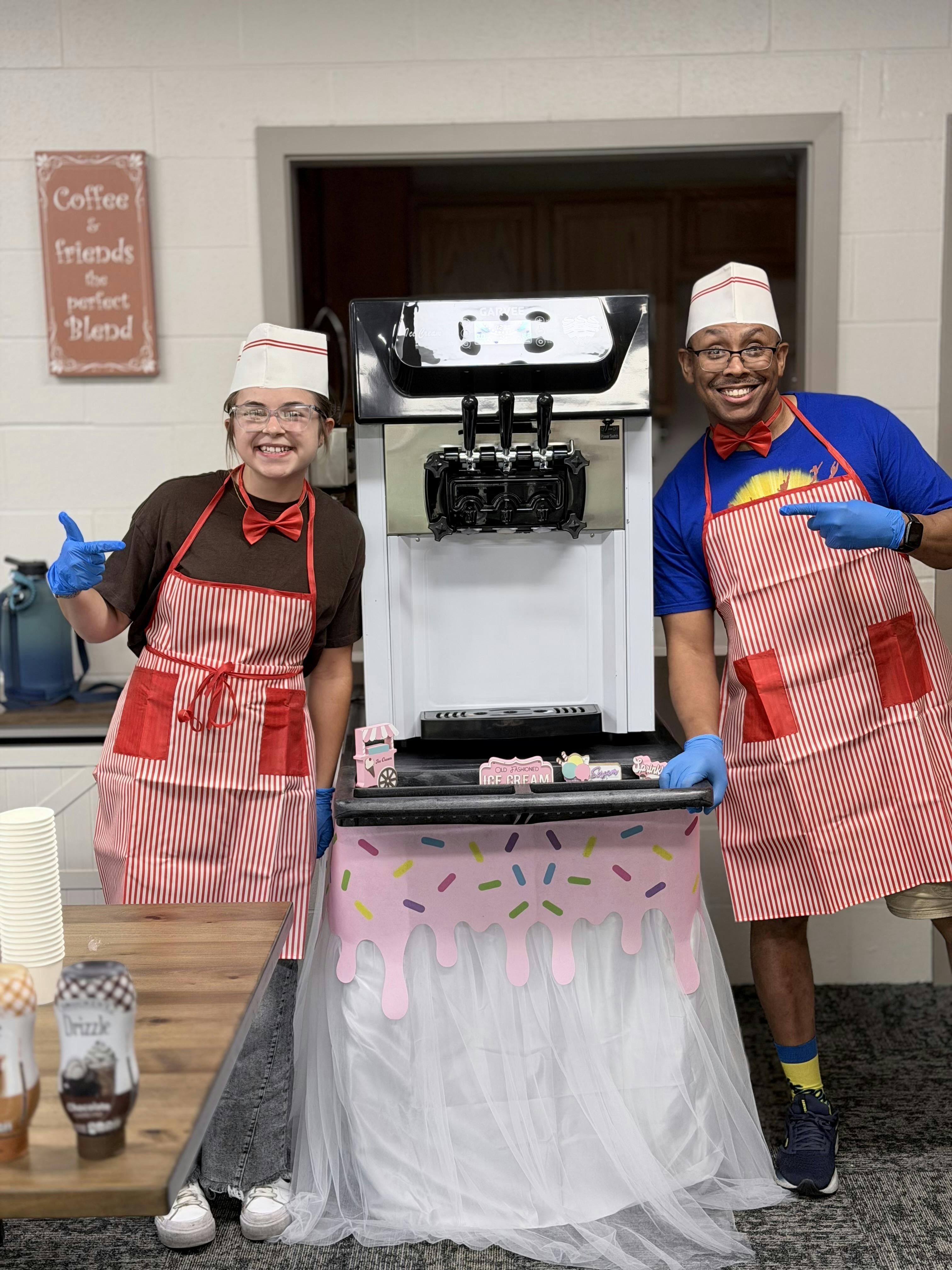 Two people wearing aprons and hats standing next to an ice cream machine