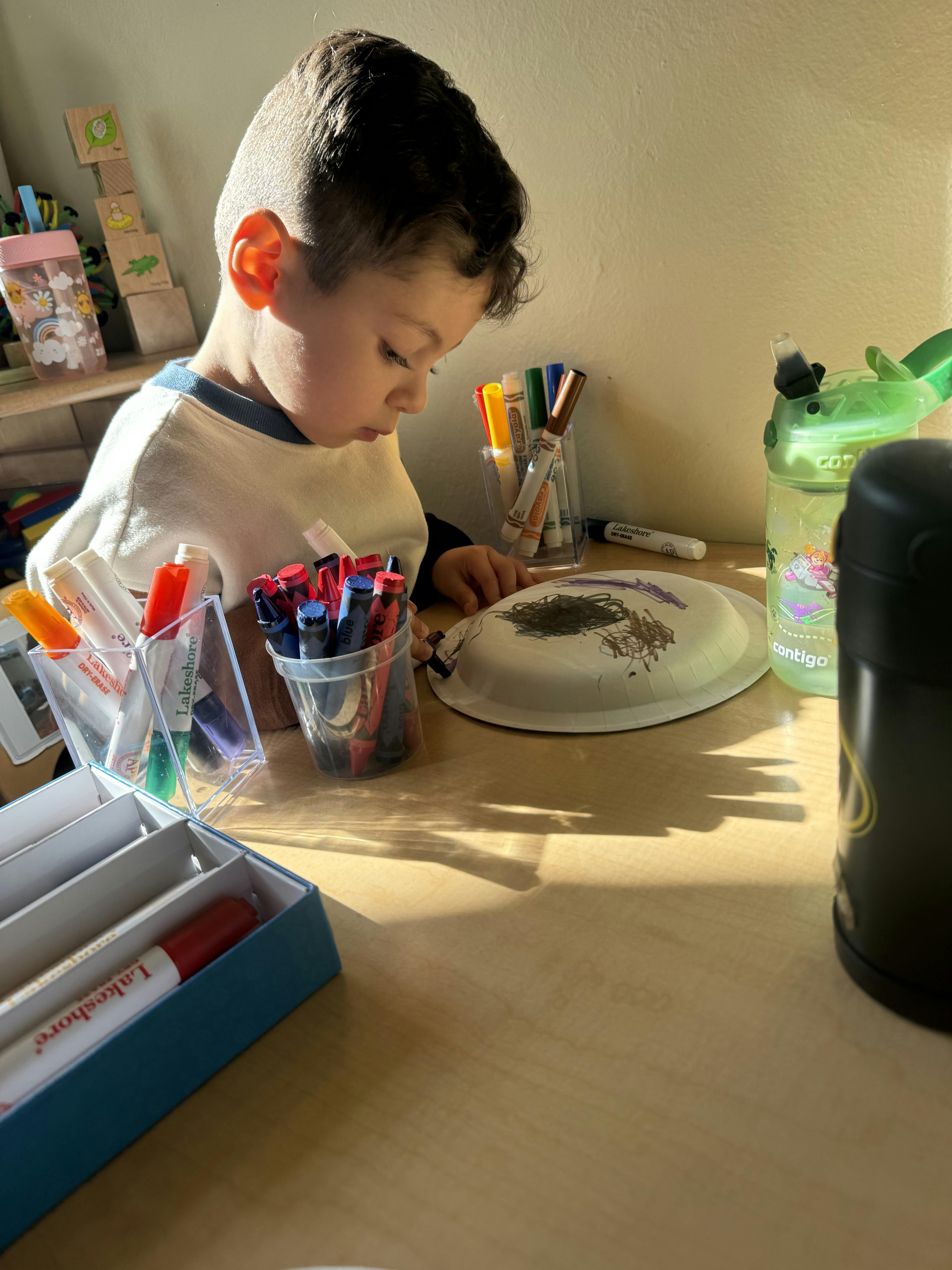 Child drawing on a paper plate with crayons and markers