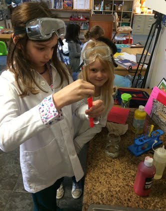 Two children in lab coats and safety goggles doing a science experiment