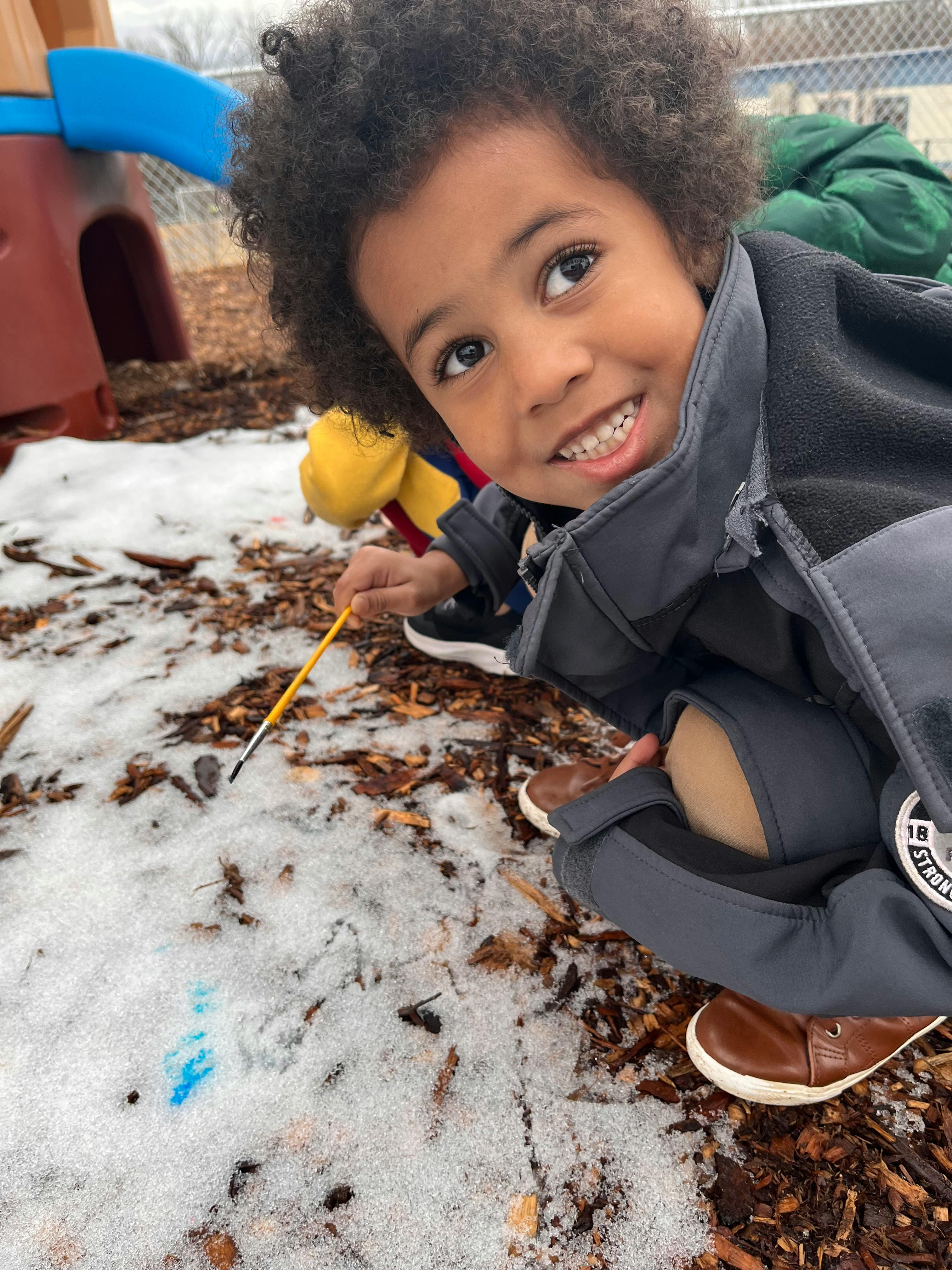 Child holding a paintbrush over snow and leaves