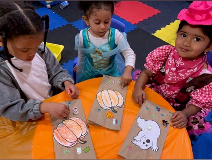 Three children decorating paper bags with Halloween-themed cutouts