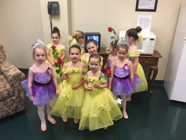 Group of children in yellow and purple dresses with tiaras and roses