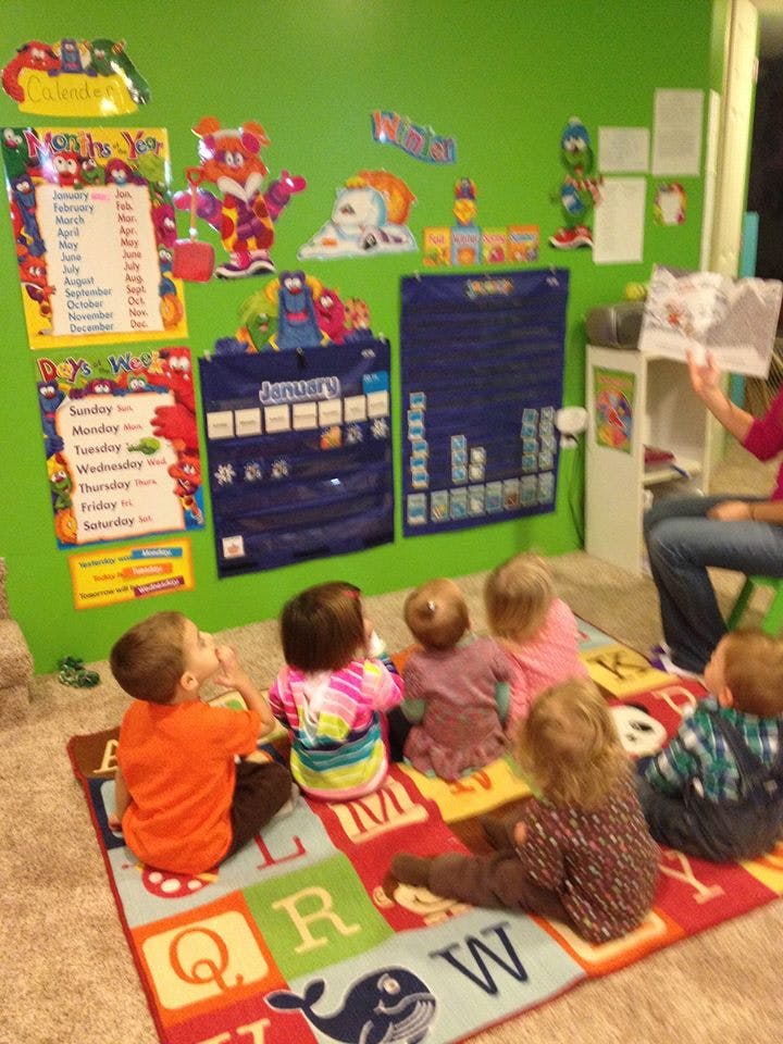 Adult reading to a group of children sitting on an alphabet rug in a classroom