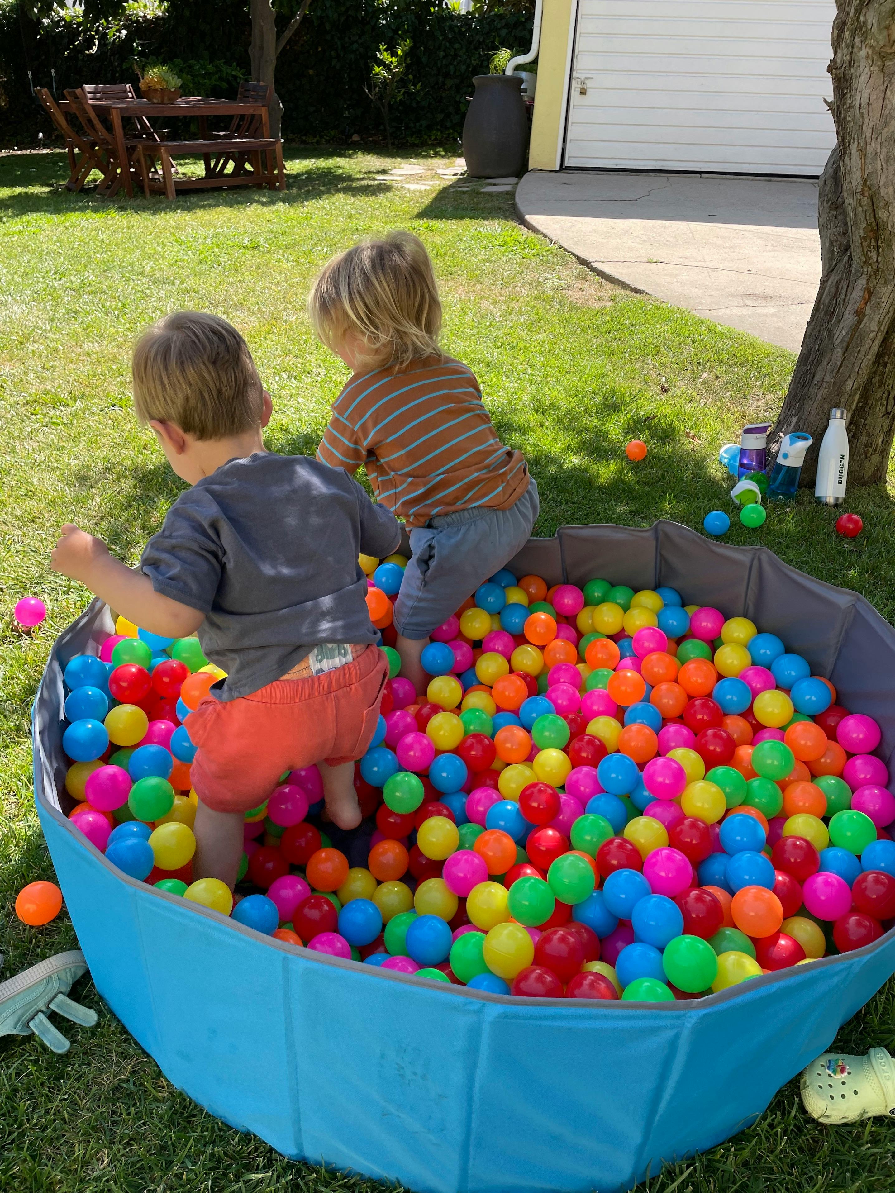 Two children playing in a ball pit outdoors