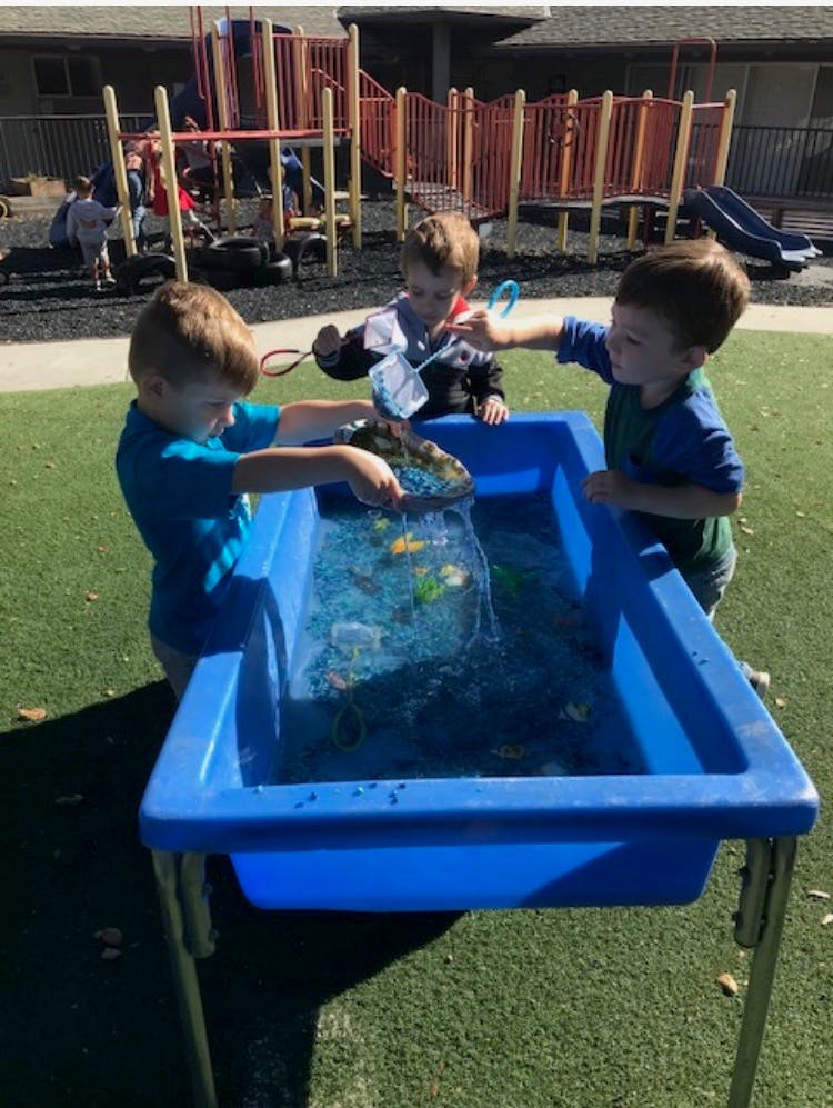 Three children playing with a water table outdoors
