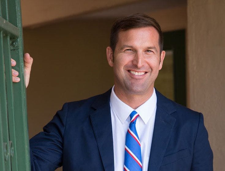 Smiling man in a suit and tie holding a green door frame