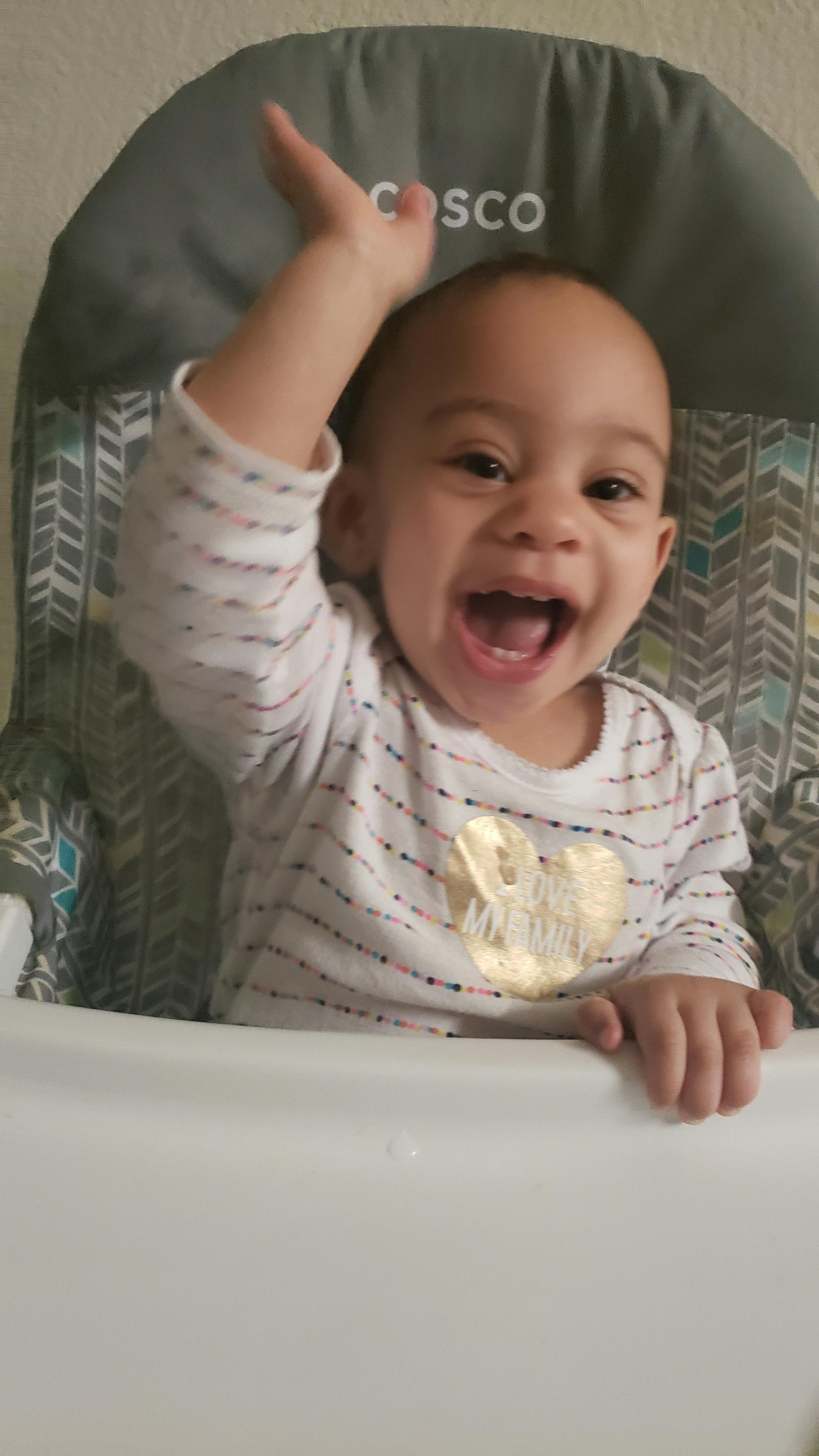 Child in a high chair with one arm raised