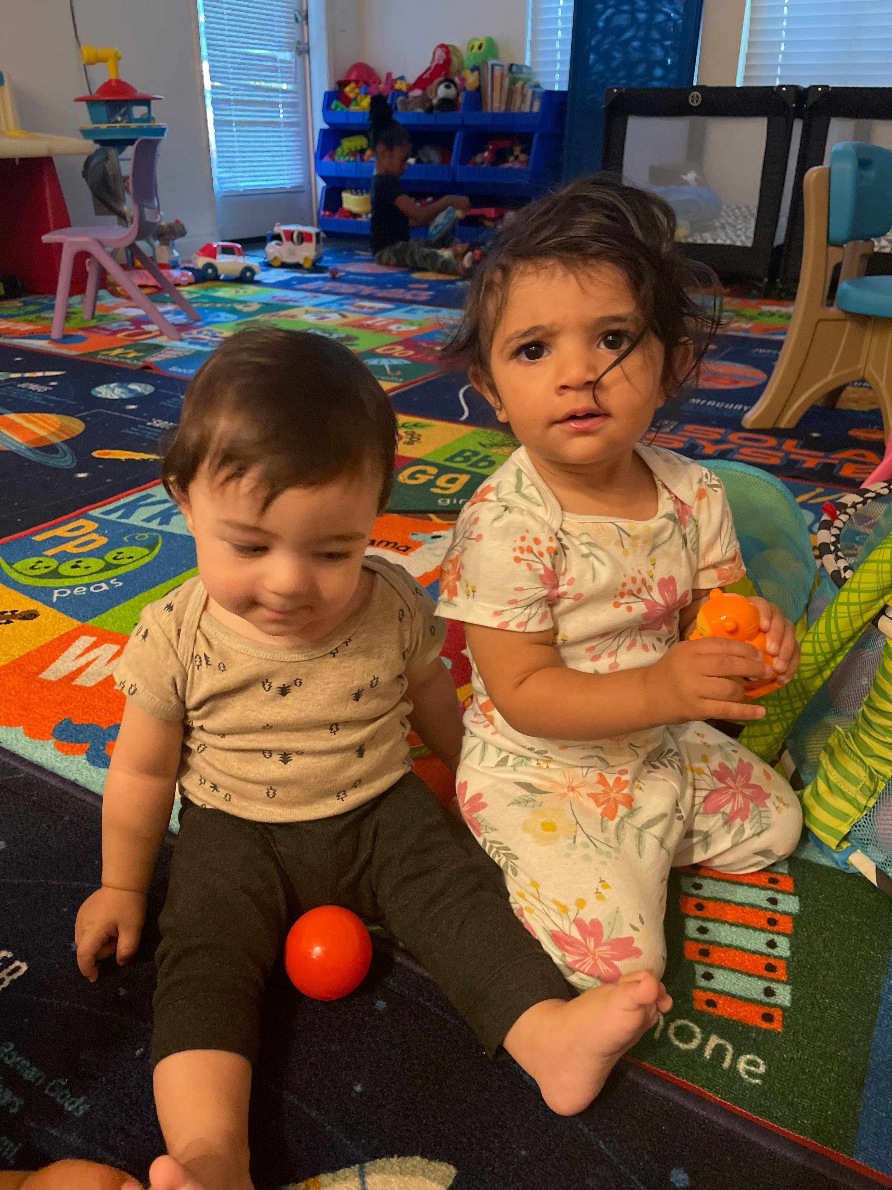 Two children sitting on a colorful playmat with toys