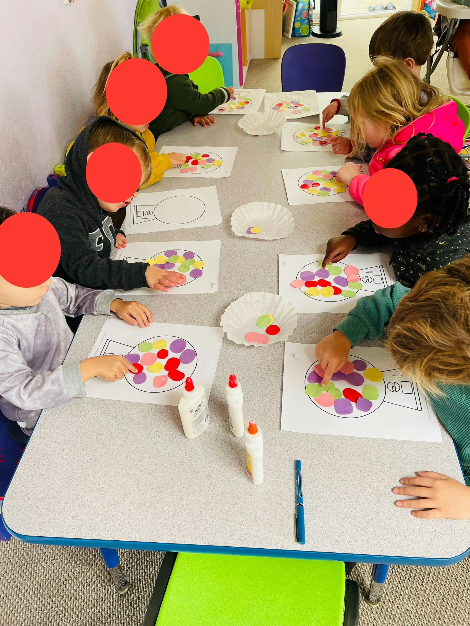 Children at a table doing an art activity with colorful paper shapes