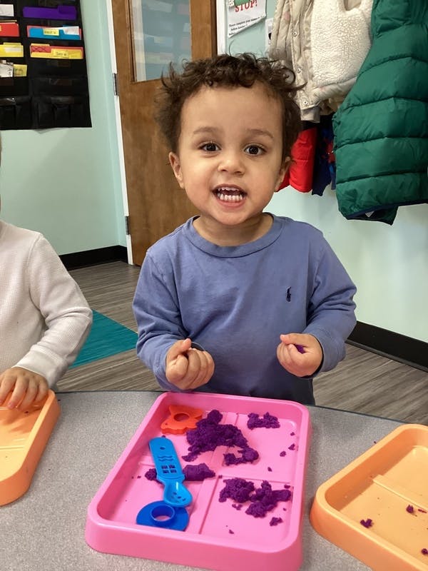 Child playing with purple kinetic sand in a pink tray