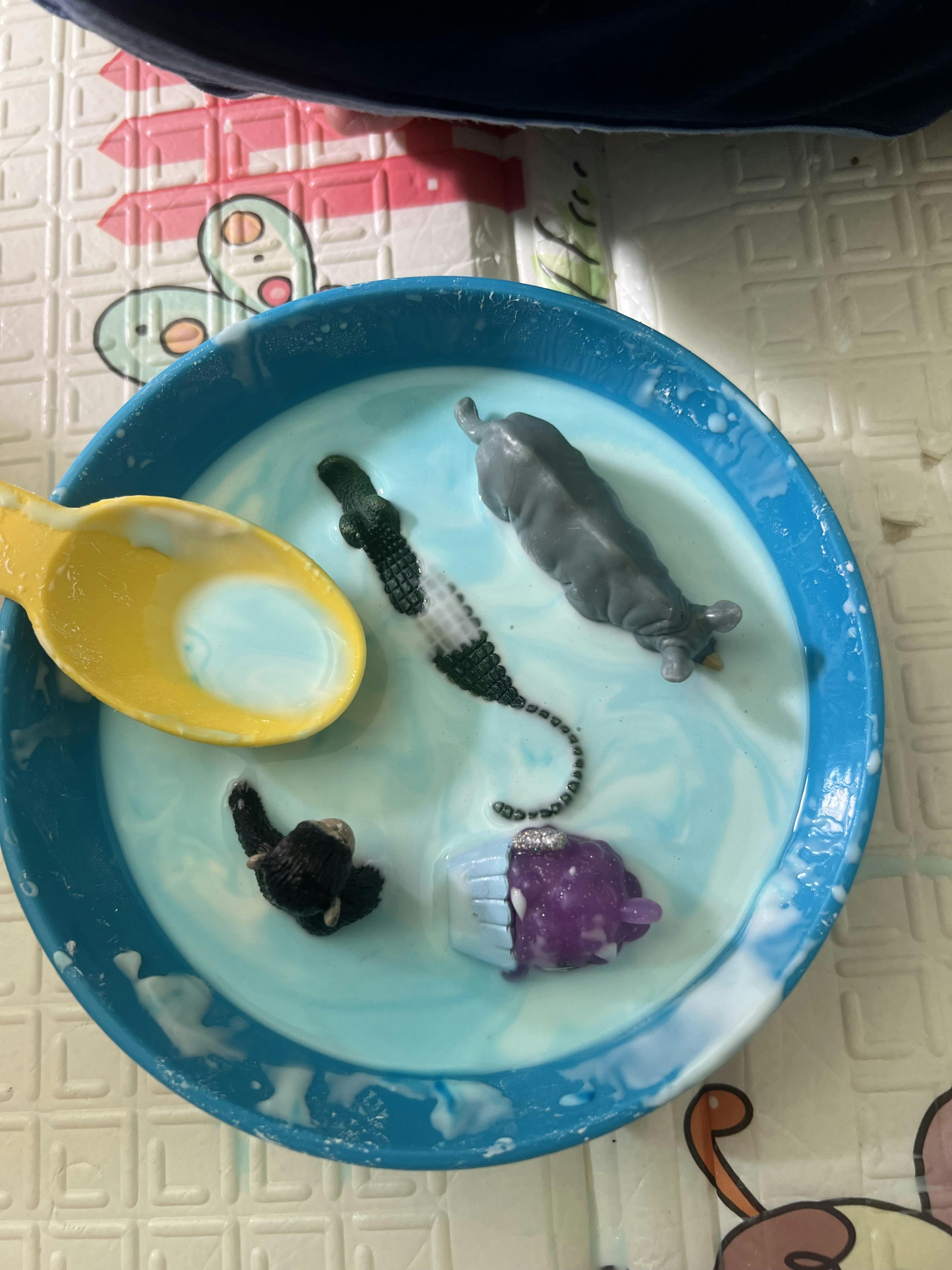 Small plastic animal figures and a spoon in a blue bowl of milk