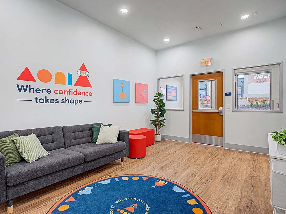Lobby area with a gray couch, a blue circular rug, and a wall decal that says "Where confidence takes shape"
