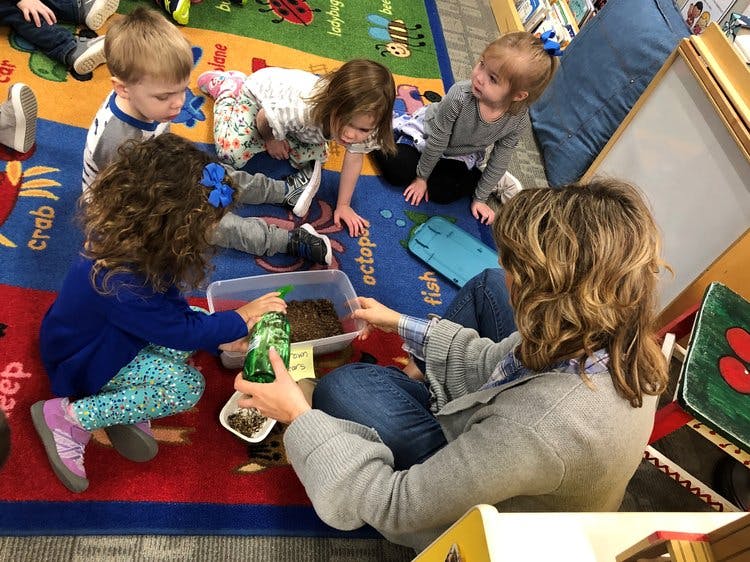 Adult and children on floor playing with container of dirt