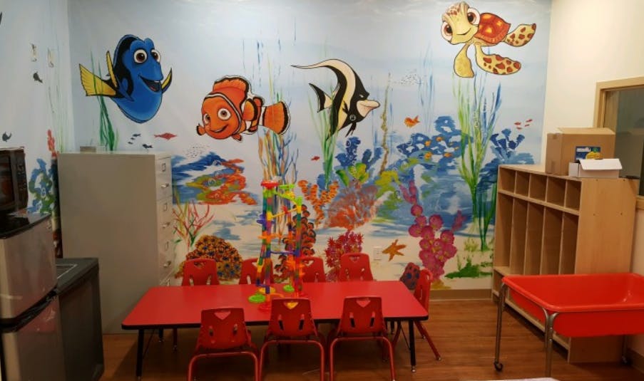 Classroom with ocean-themed wall mural and red tables and chairs