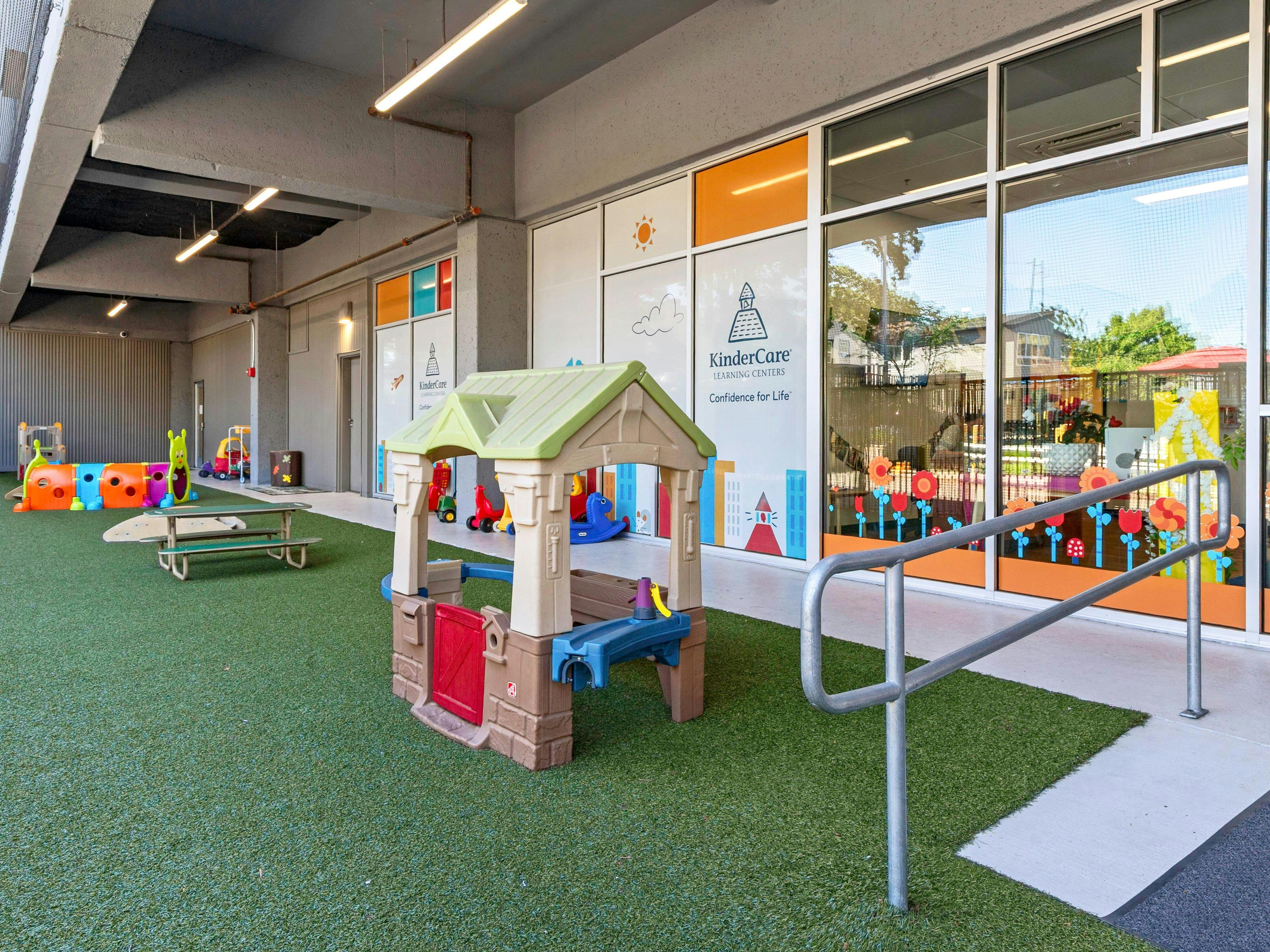 Outdoor play area with artificial turf, playhouse, and various colorful toys