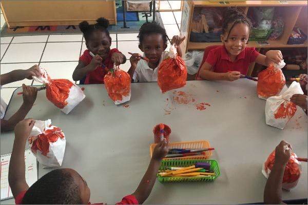 Children painting paper bags at a table