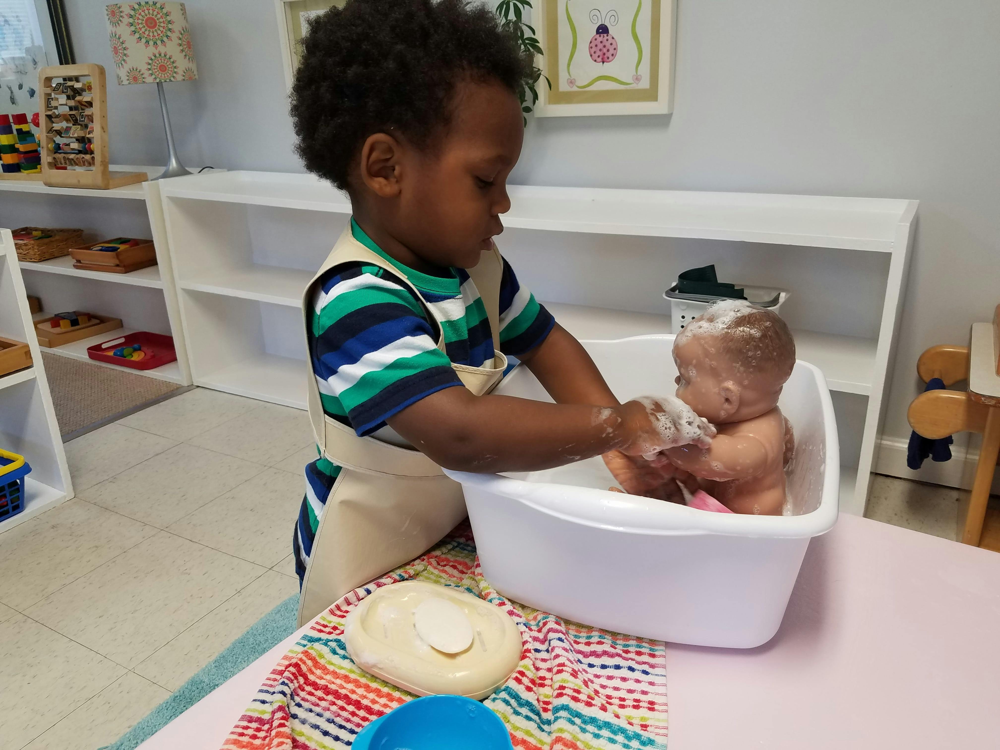 Child in an apron washing a doll in a small tub