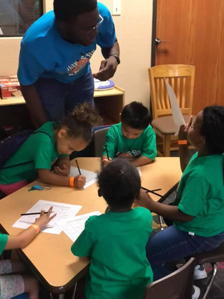 Adult person standing over children seated at a table doing schoolwork