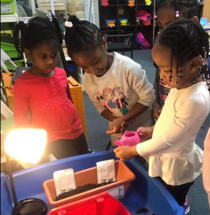 Three children watering plants in a classroom