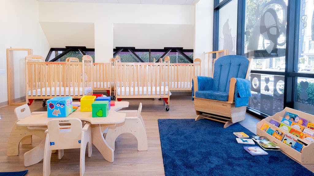 Cribs, a child-sized table with chairs, a rocking chair, and a bookshelf with books
