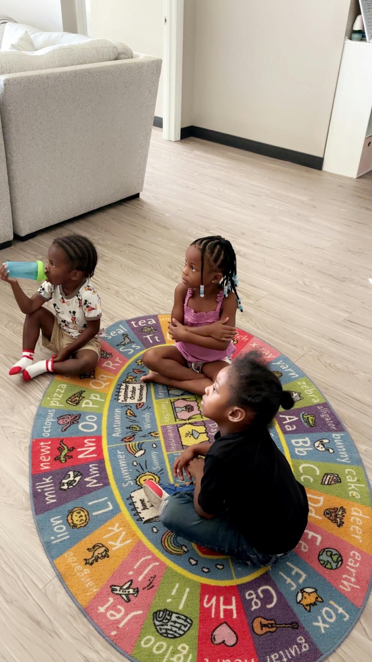 Three children sitting on a colorful alphabet rug