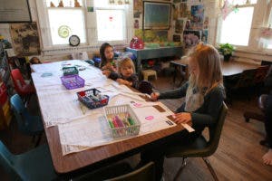 Three children sitting at a table with art supplies