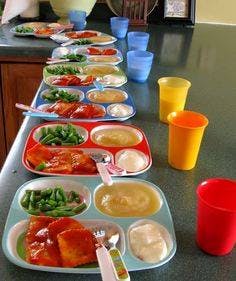 Multiple trays of food with green beans, applesauce, and chicken