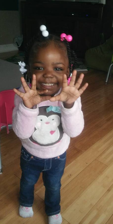 Child in a pink shirt with a penguin design holding hands up