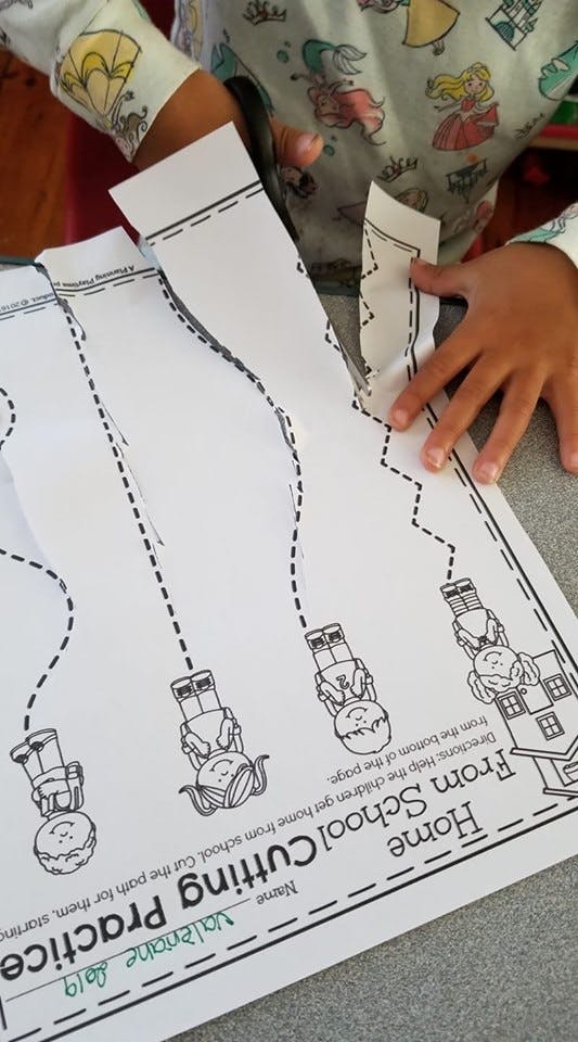 Child cutting paper along a dotted line on a worksheet