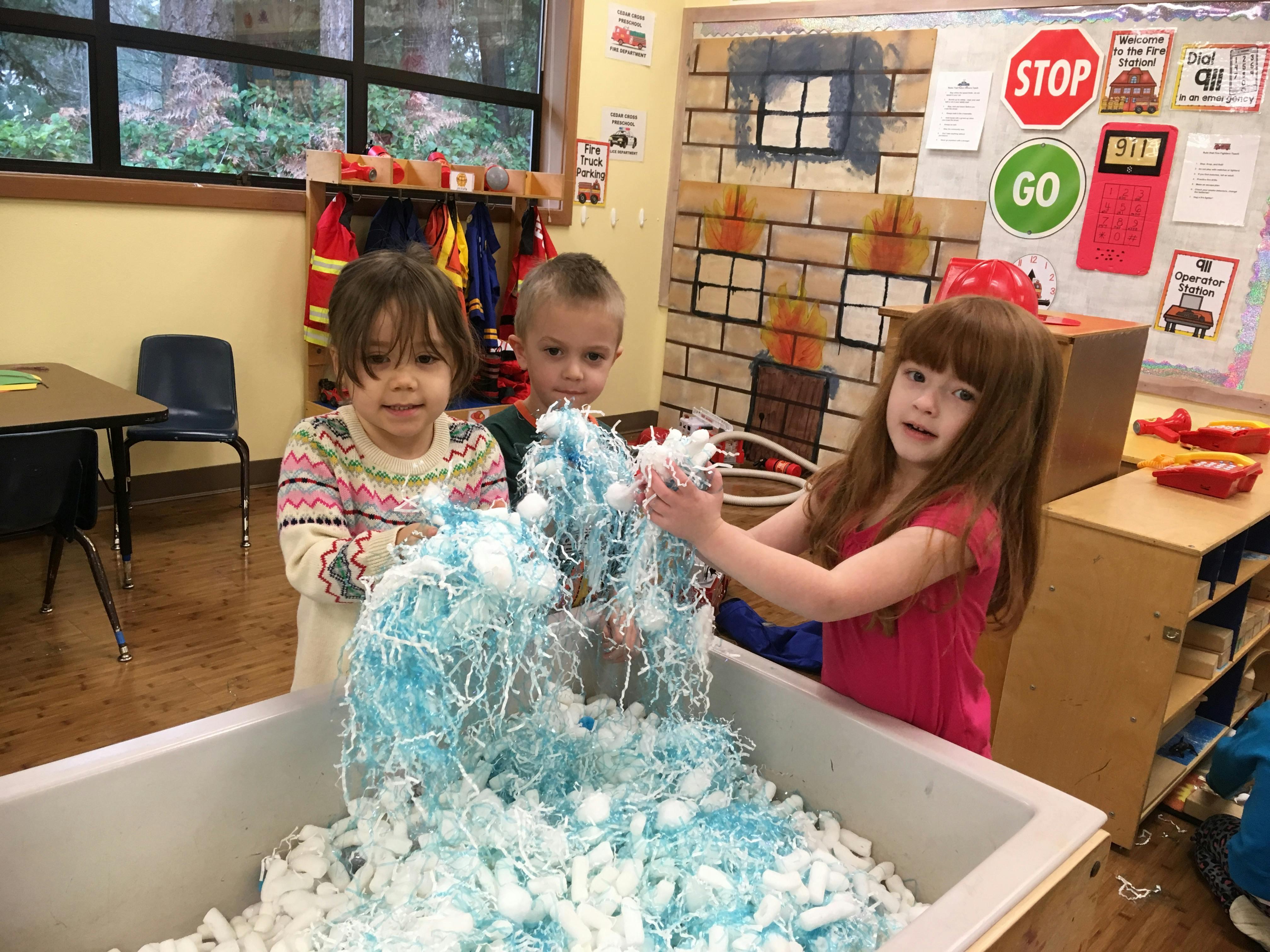 Three children playing with shredded paper in a bin