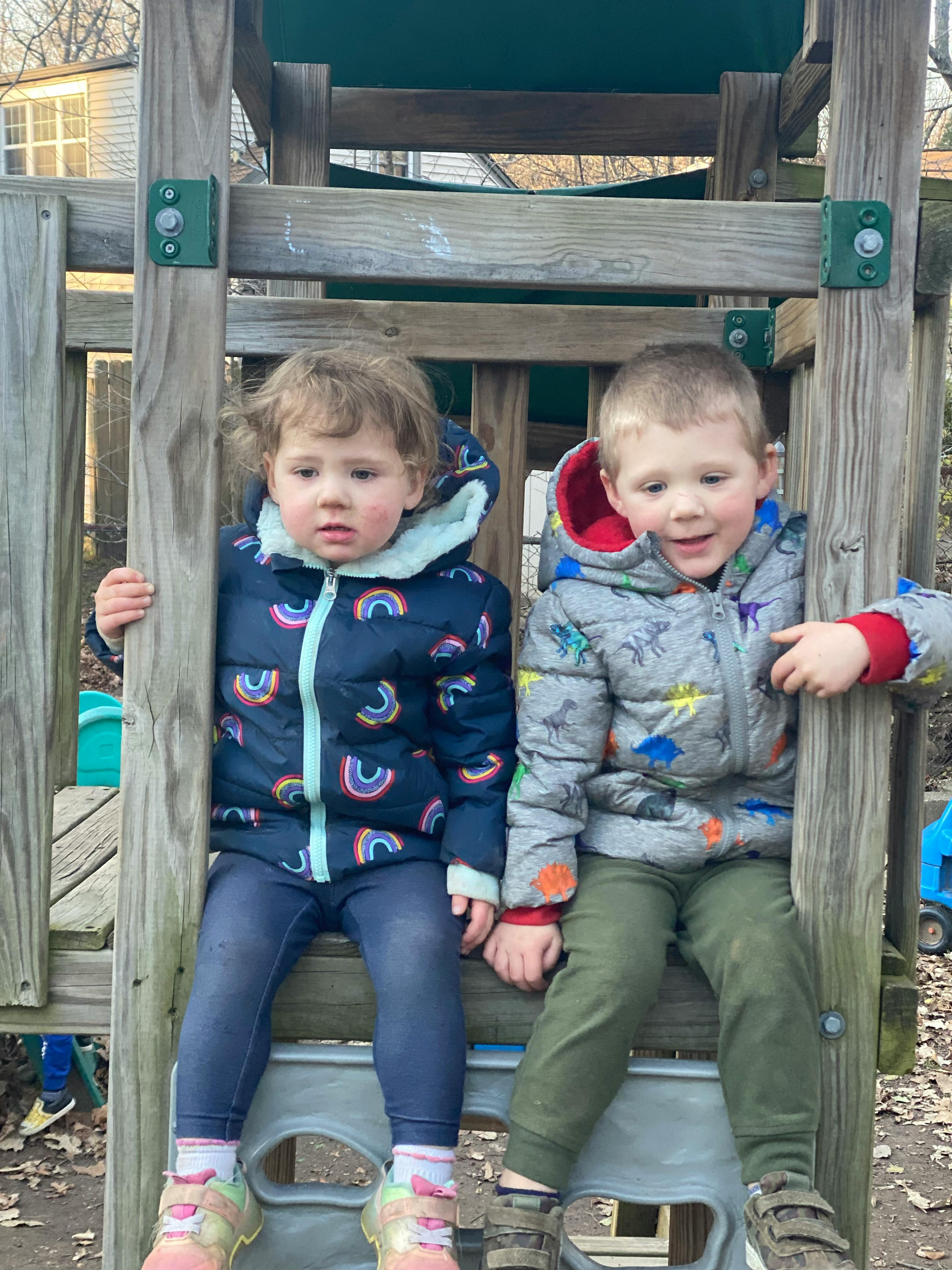 Two children sitting on a wooden play structure