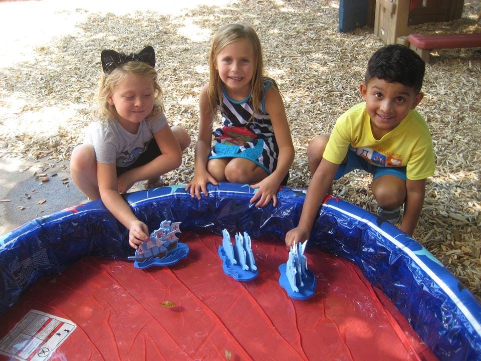 Three children playing with toys in a small red and blue pool