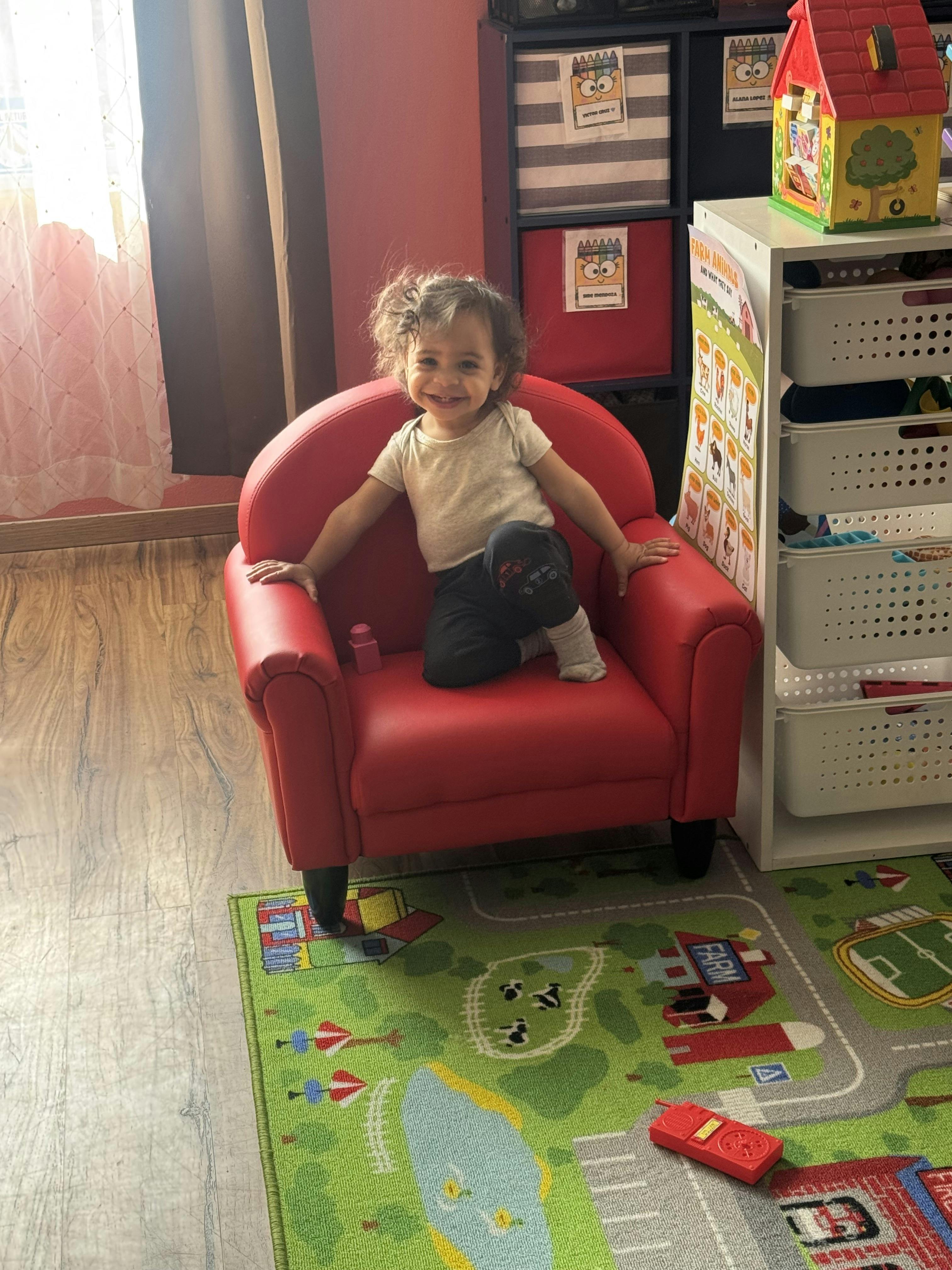 Child sitting in a small red armchair in a playroom
