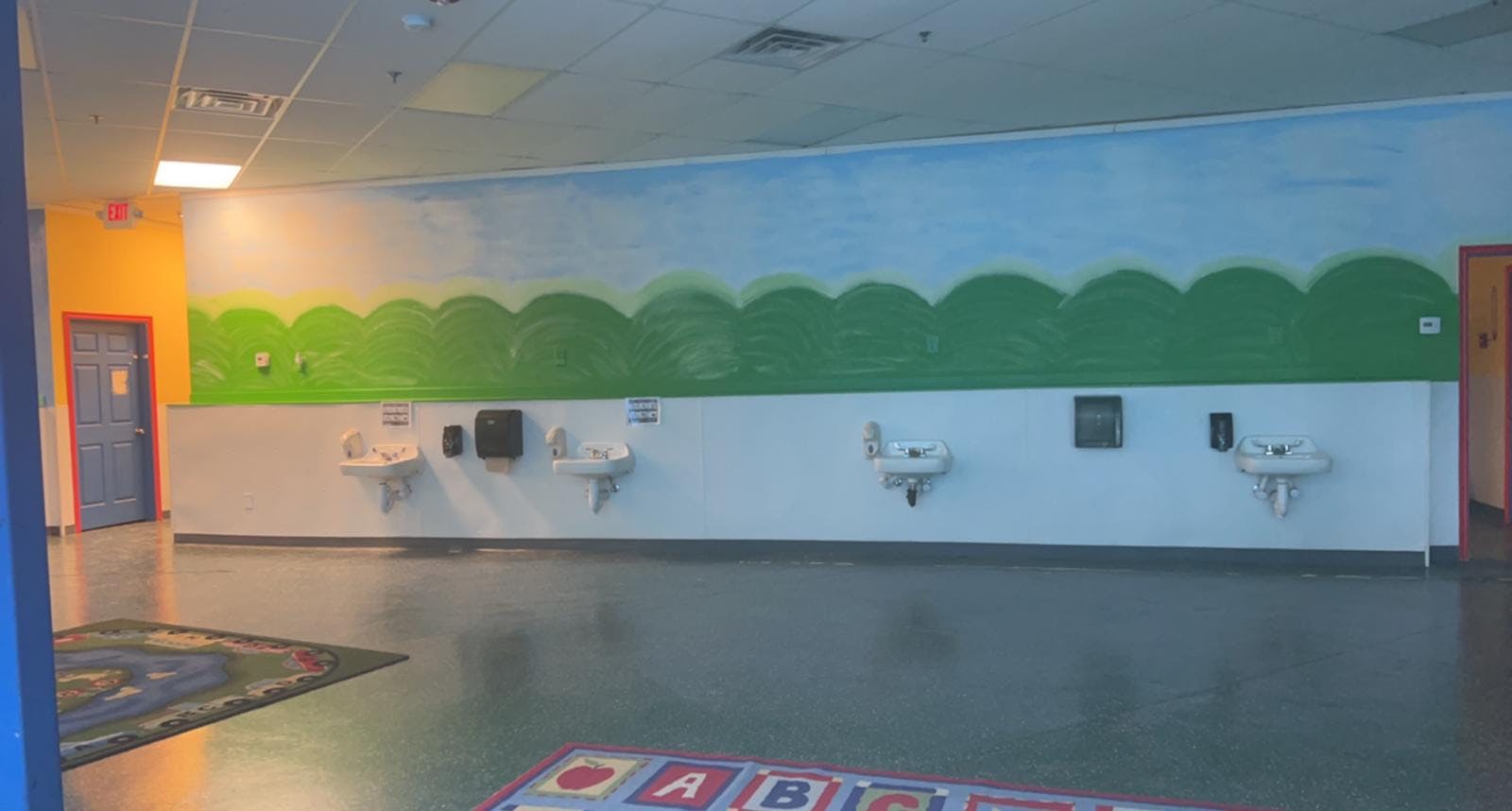 Children's room with sinks and a mural of green hills under a blue sky
