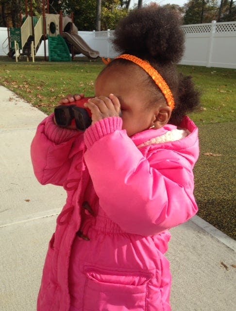 Child in a pink coat looking through binoculars on a playground
