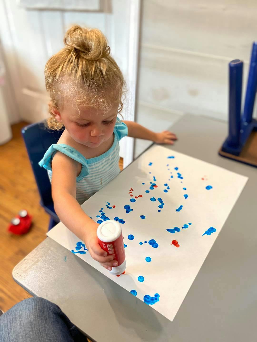 Child making blue and red dots on paper with a marker
