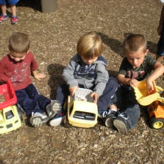 Three children playing with toy trucks outdoors