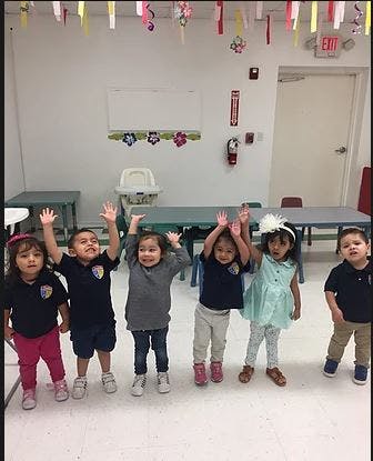 Six children standing in a classroom with their hands raised