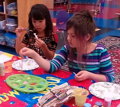 Two children painting small objects at a table