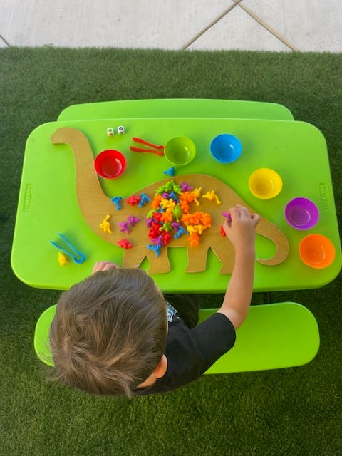 Child playing with dinosaur-shaped board and colorful dinosaur figures
