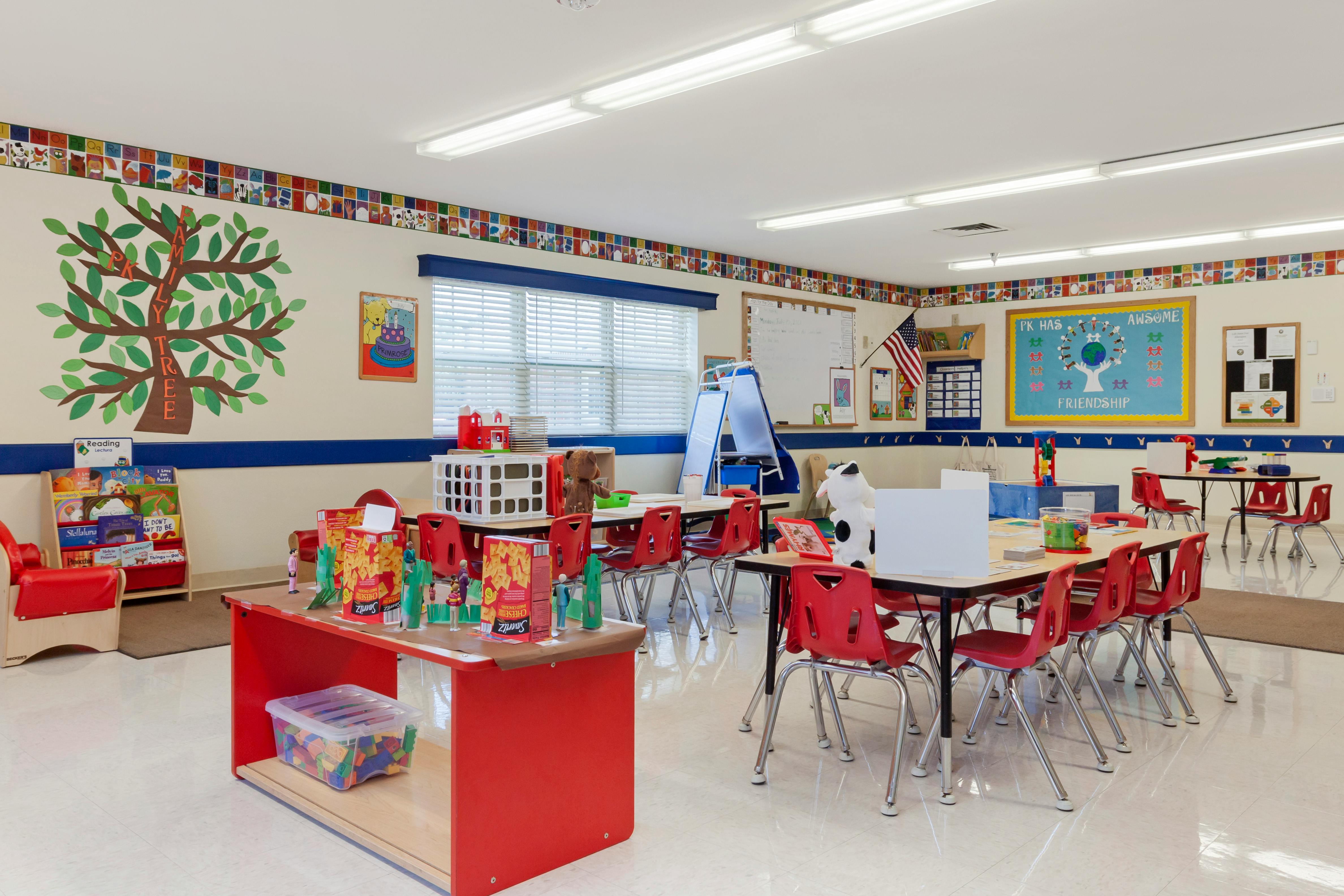 Colorful classroom with small tables and red chairs, children's books, and wall decorations
