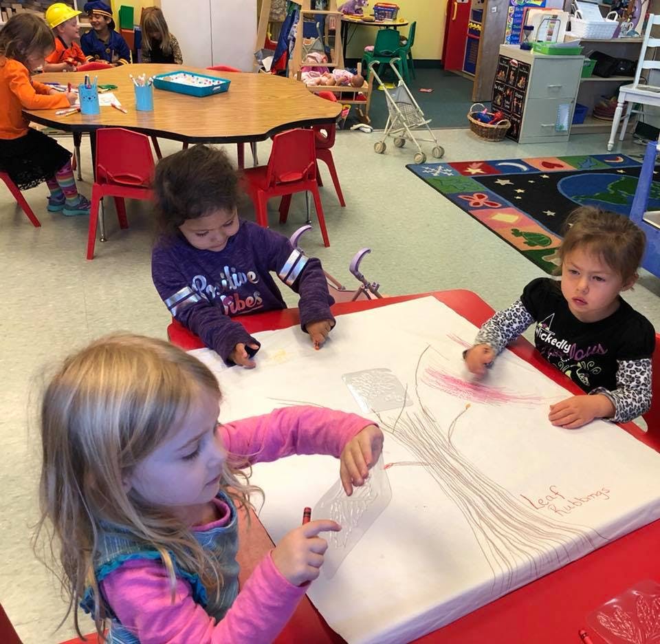 Three children drawing at a table in a classroom