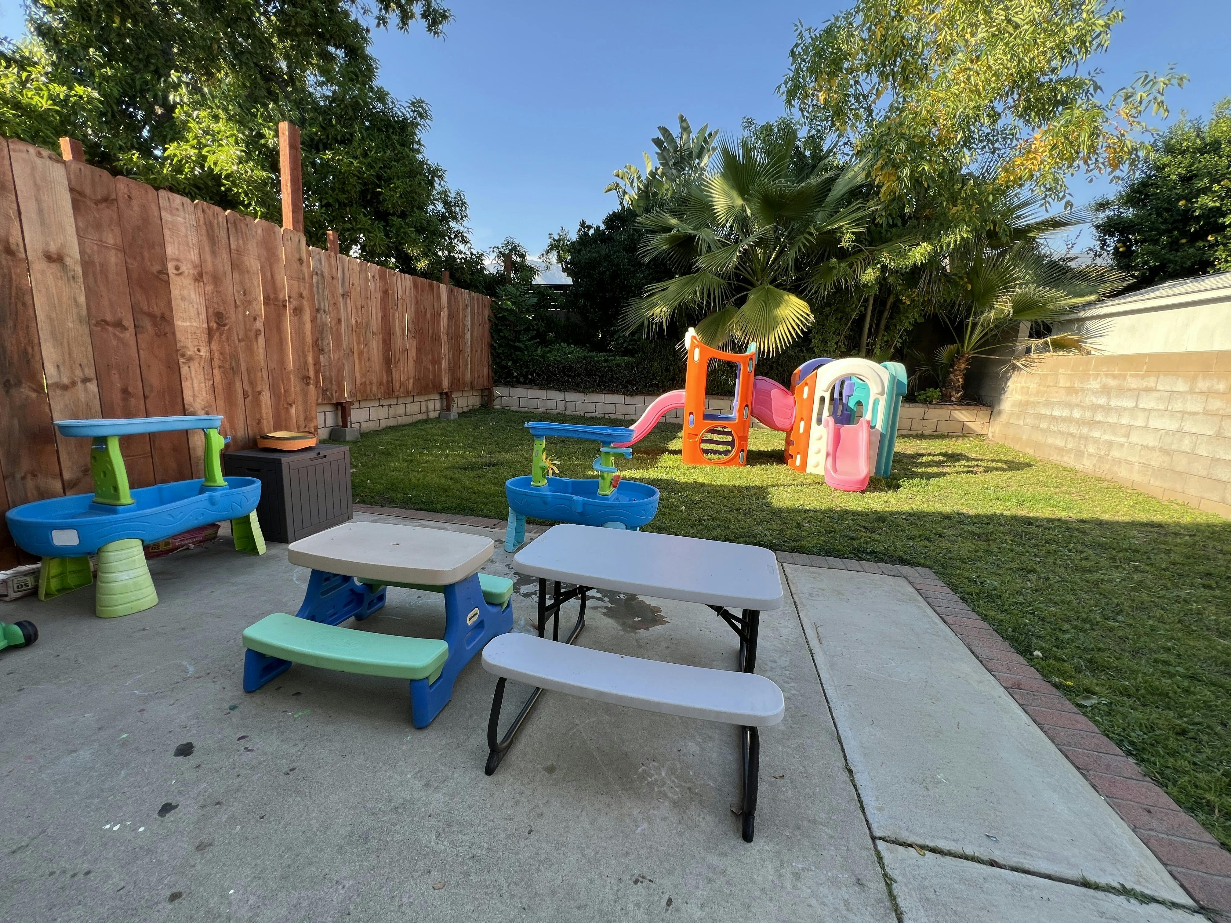 Backyard with a playground set, water table, and two picnic tables