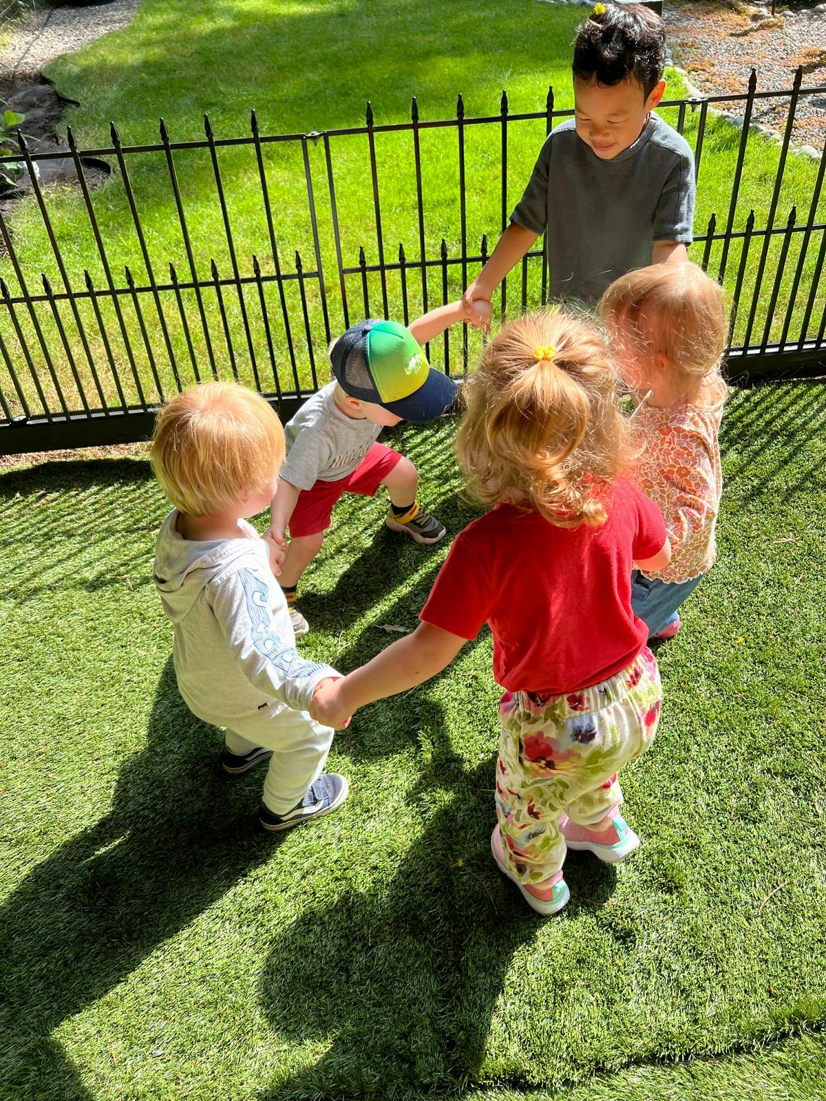 Four children holding hands in a circle on grass