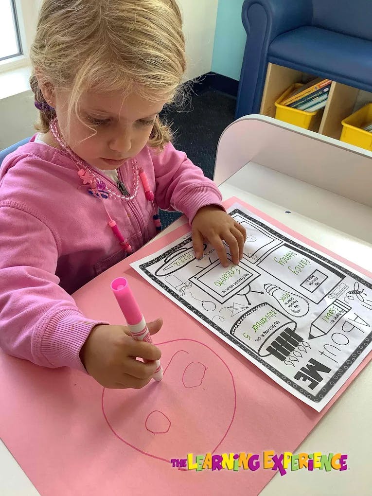 Child drawing on pink paper with a marker